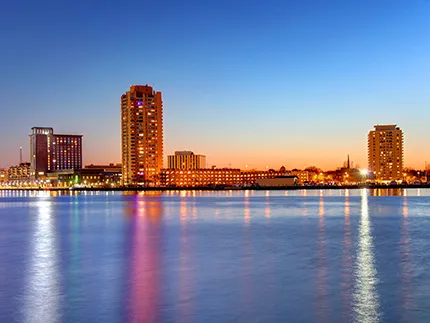 Tall buildings of a city skyline show reflections on the river in the foreground with sunset in backgroung
