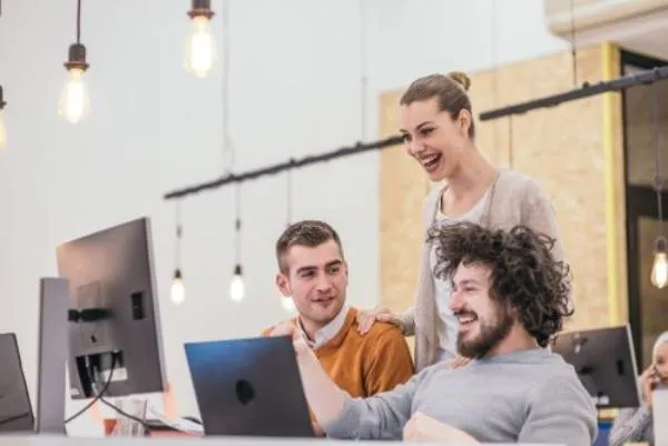 Three people laughing around a laptop