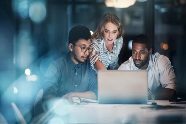 Three people facing the camera looking a laptop