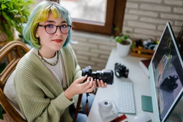 Funky girl with multicolored hair at a computer holding a camera
