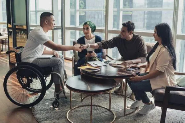 Man in wheelchair shaking hands with group seated around a small table