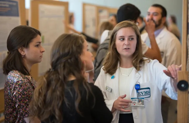 A picture of a medical student explaining her research poster to 2 other women.