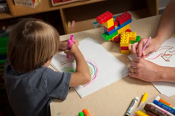 A fellow observes a child drawing.