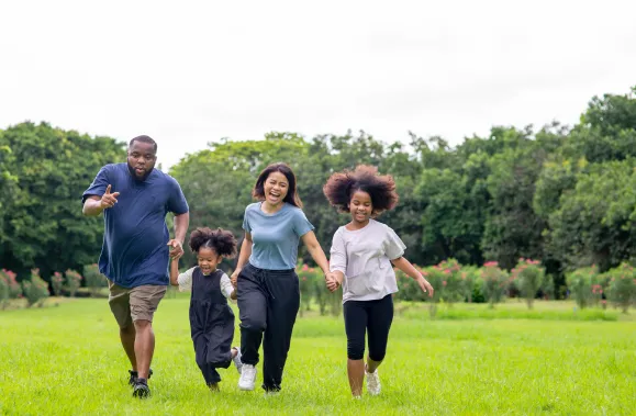 Happy mixed race family two parents with cute daughter holding hands and running together in the park.