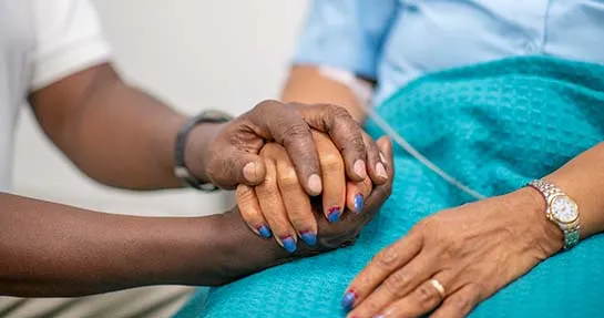 Elderly woman is comforted by a medical professional. Focus is on their hands. The medical staff is holding the woman's hand.