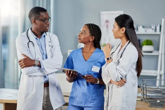 Three doctors and a woman in blue scrubs discuss a report