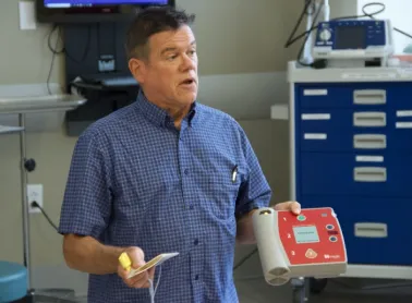 A man holding a heart device and talking to students