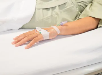 Close up saline drip for patient in hospital room. Patient on the bed.