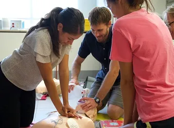 Three students practice performing CPR, and the use of an AED and Oxygen Bag Valve Mask on a manikin.