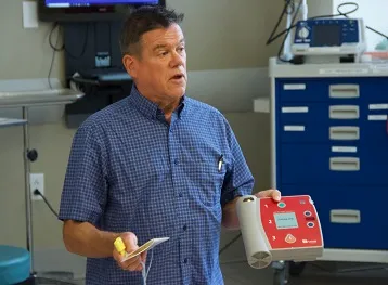 A man instructs a class while holding an AED.
