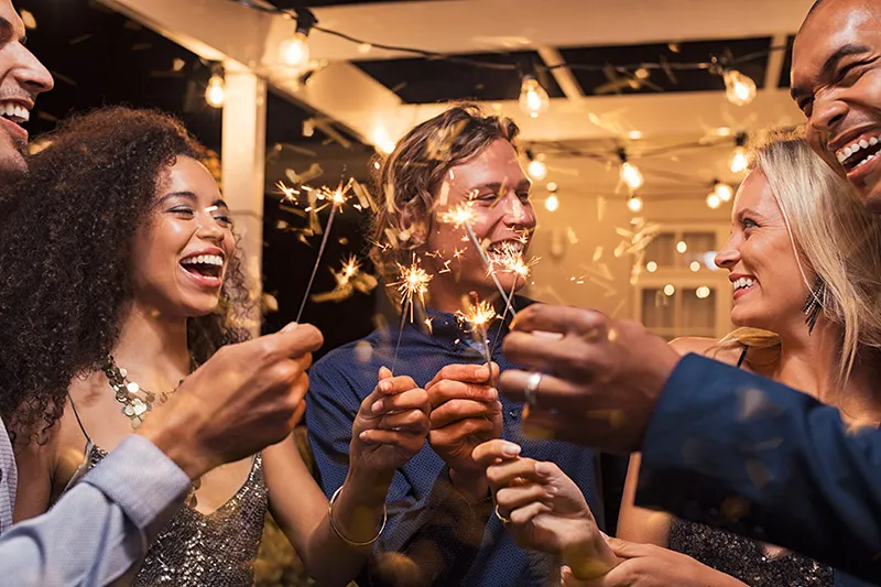 Five friends laugh and smile at a party while holding sparkers
