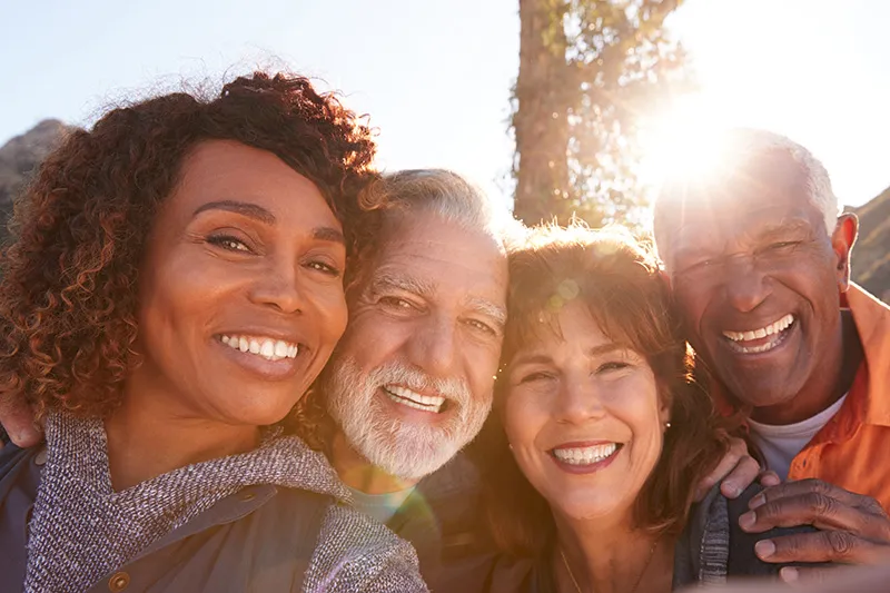 A diverse group of four seniors are being active outdoors. They are smiling at the camera.