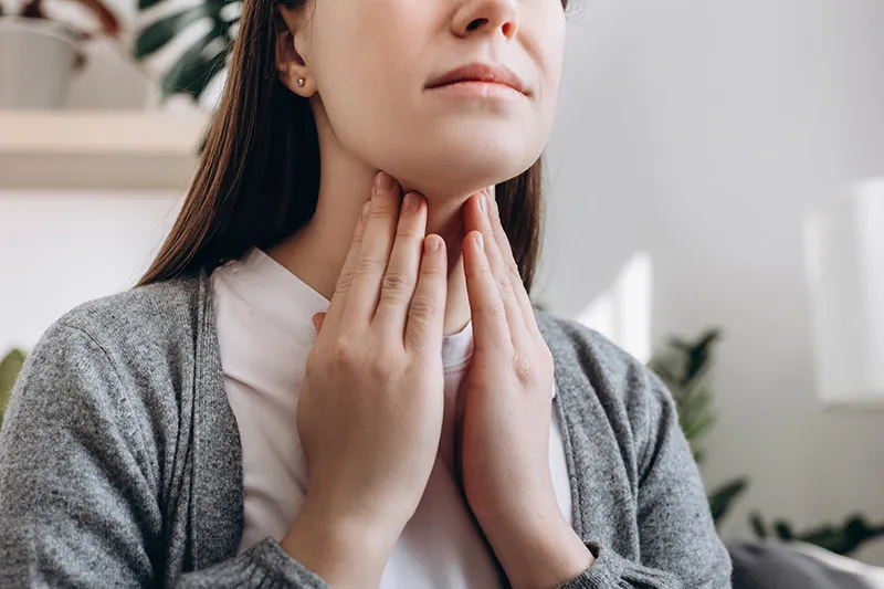 A woman uses both hands to touch her neck. She looks worried.