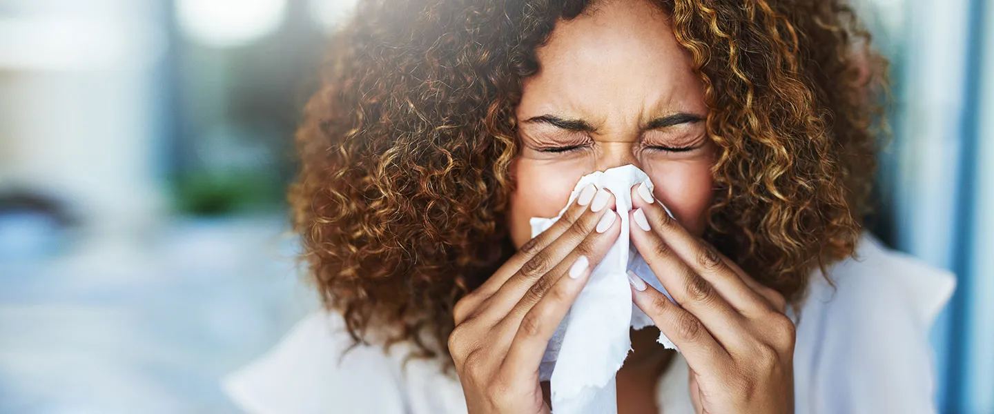 A woman has clogged sinuses and blows her nose using a tissue