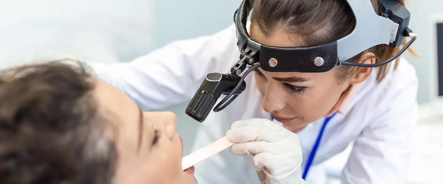 A doctor examines a patient's throat using a light and a tongue depressor