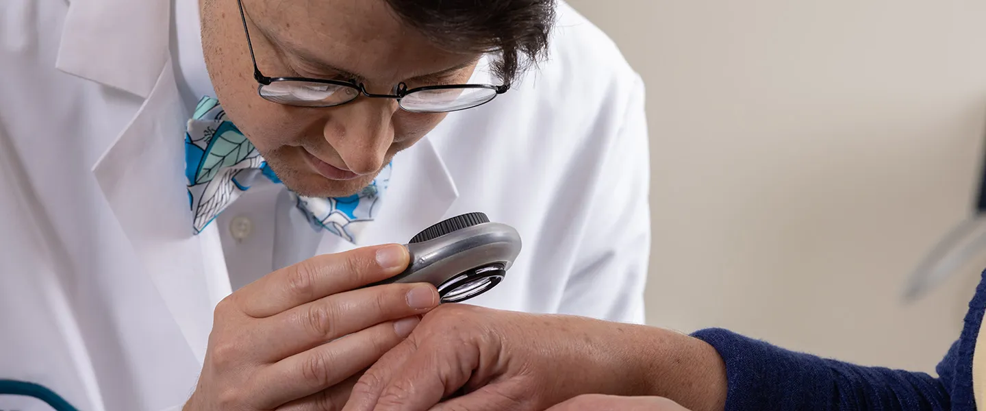 Clinton Enos, MD examines the hand of a dermatology patient.