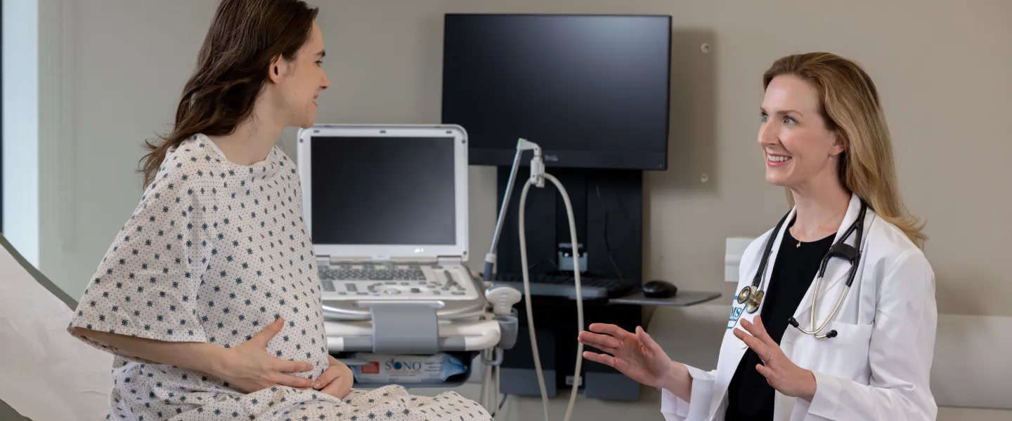 Dr. Robbins smiling with pregnant patient in a doctor's clinic.