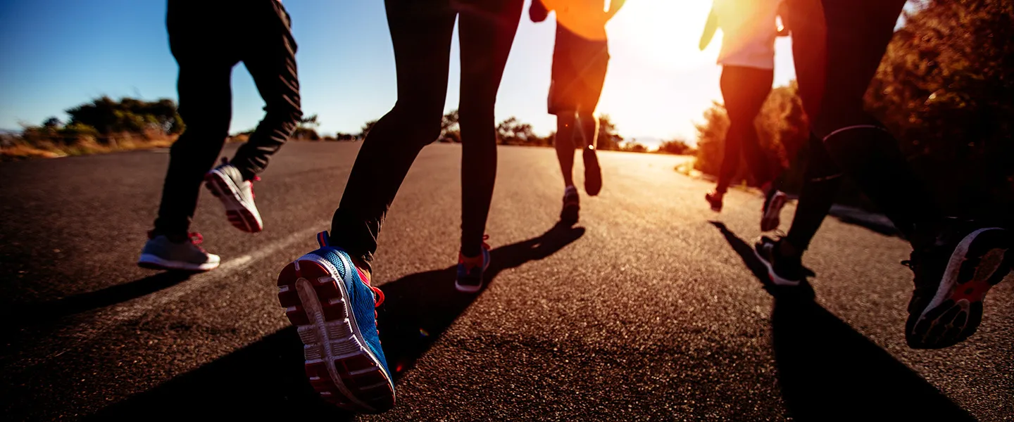 Photo of legs of runners on pavement with the sun in the background