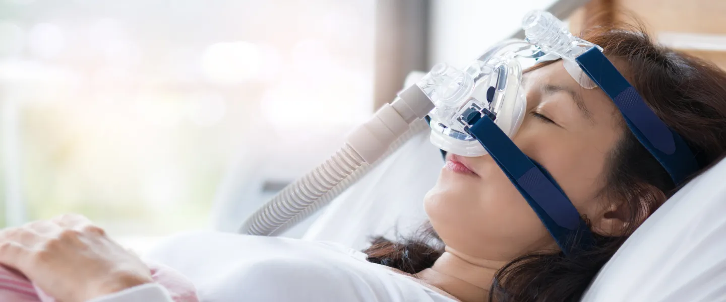 Senior woman using cpap machine to stop choking and snoring from obstructive sleep apnea with bokeh and morning light background.
