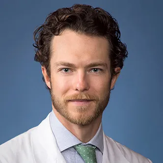 Dr. Kerr has short curly hair and a goatee, and is wearing a blue shirt and green tie under a white medical coat.