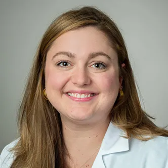 Dr. Waller has long straight light brown hair, is wearing a white medical coat, and is smiling at the camera.