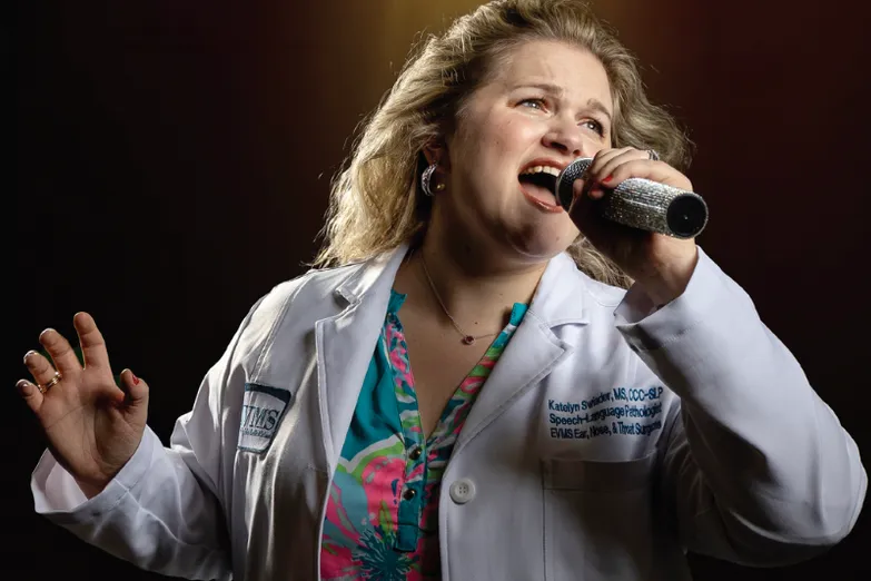 Katelyn Swiader wearing a white coat while holding and singing into a microphone