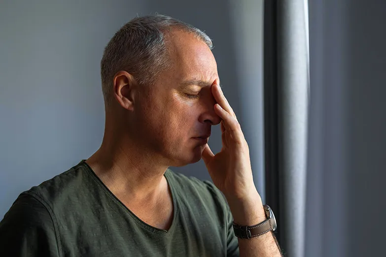 A man with gray hair wearing a gray shirt holds his hand to his face, in pain from nasal polyps.