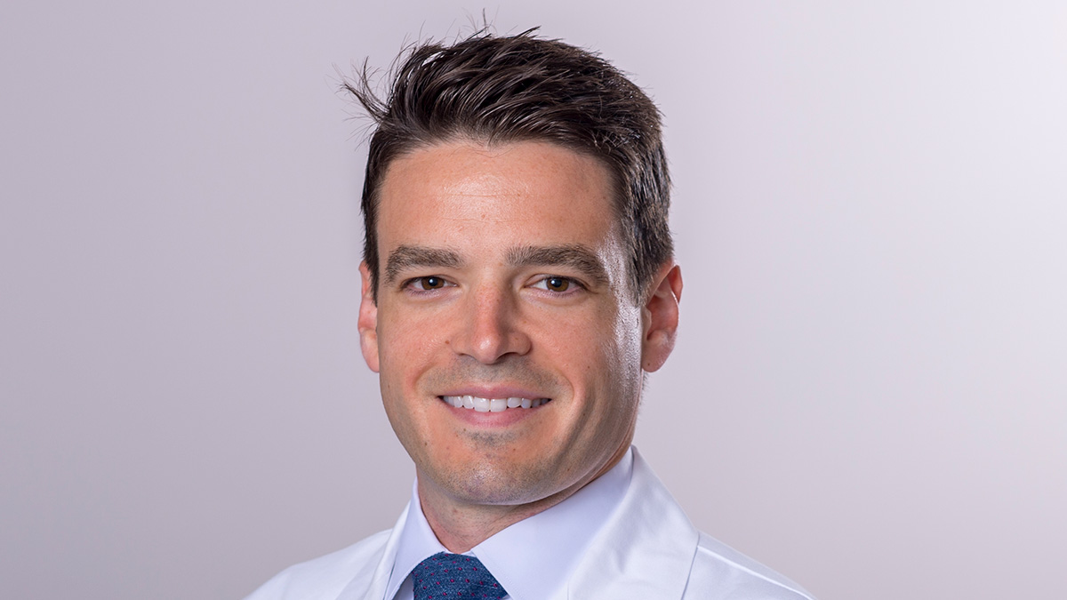 Dr. Dougherty has short brown hair, is wearing a blue tie with white shirt and white medical coat, and is smiling at the camera