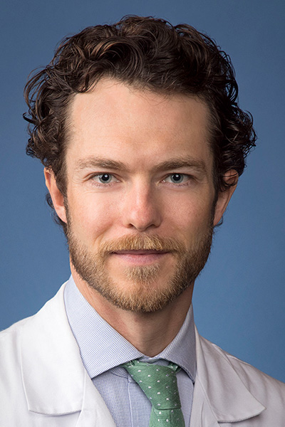 Dr. Kerr has short curly hair and a goatee, and is wearing a blue shirt and green tie under a white medical coat.