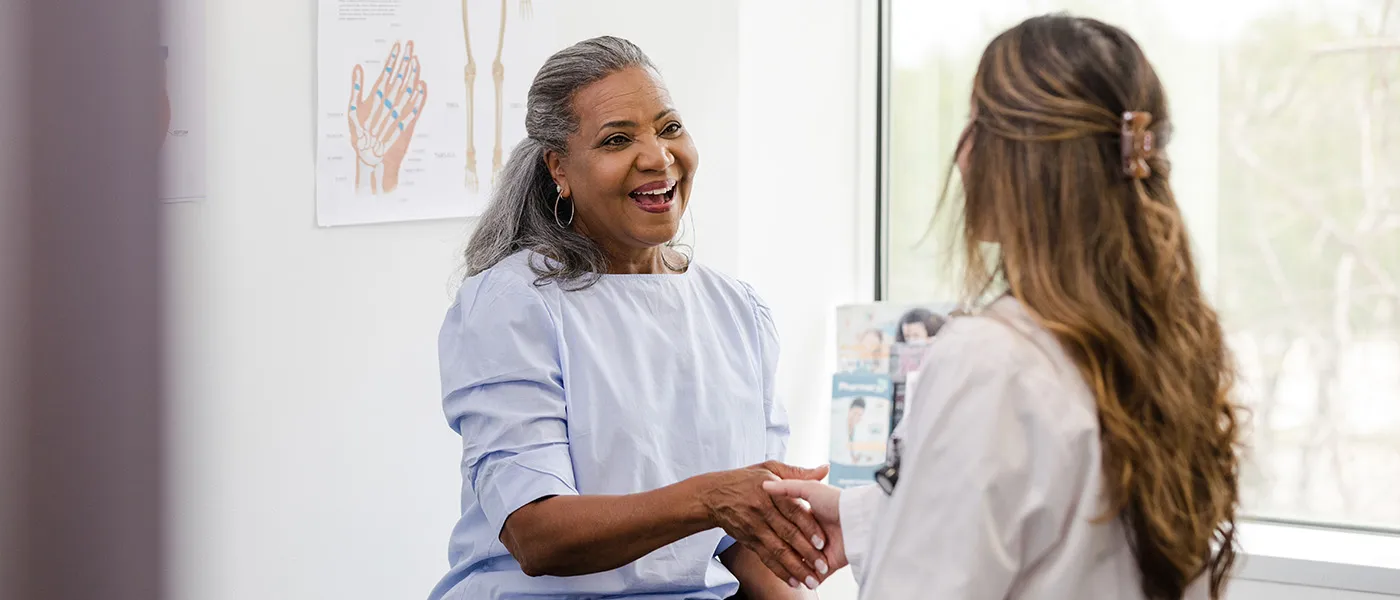 A female patient and female doctor shake hands and talk in an office.